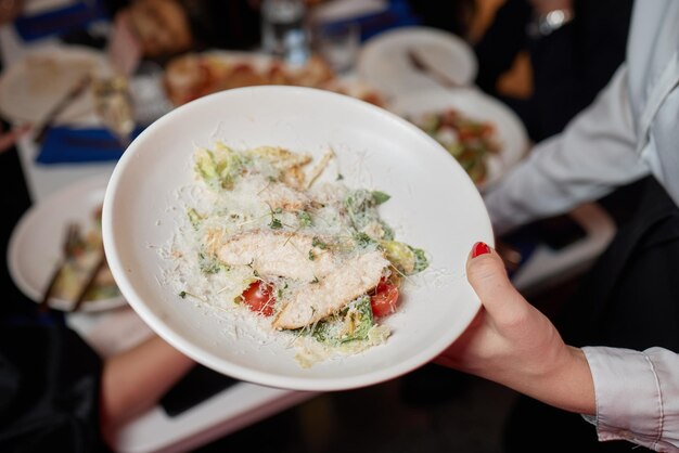 Insalata di verdure fresche con carne di pollo e pomodori. Insalata Cesare. Servito in un piatto blu. In mano a un cameriere. Servizio ristorante. Cameriere al lavoro.