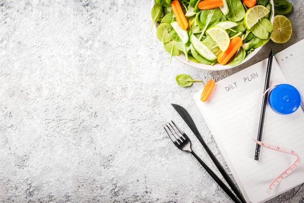 insalata di verdure fresche con forchetta, coltello e blocco note sul tavolo di pietra grigia