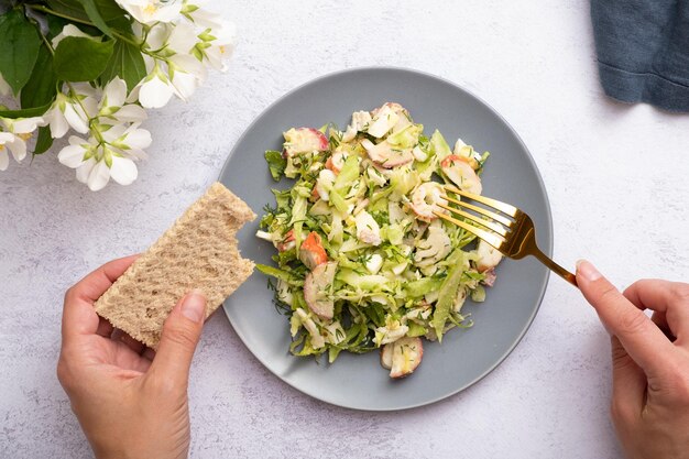 Insalata di verdure fresche e bastoncini di granchio in un piatto con mani femminili Il concetto di una sana alimentazione