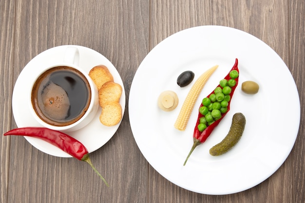 Insalata di verdure in scatola e una tazza di caffè nero con pepe rosso e cracker sui piatti