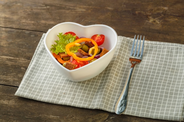 Insalata di verdure in un piatto a forma di cuore su un tavolo di legno su un tovagliolo.