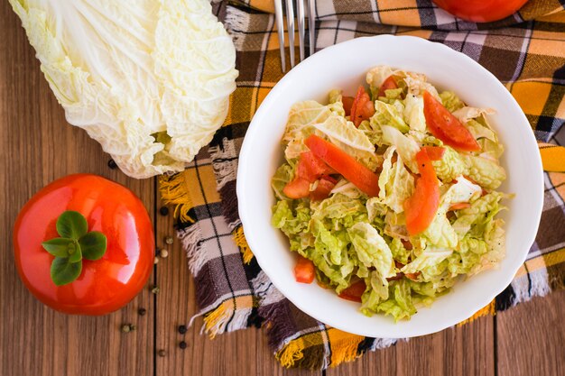 Insalata di verdure pronta da mangiare, pomodori e cavolo cinese su una tavola di legno, vista superiore