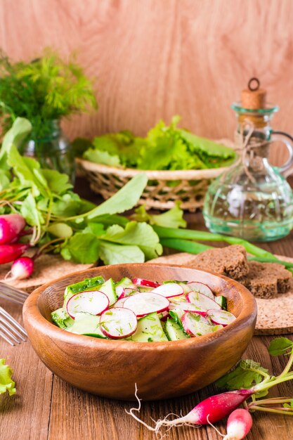 Insalata di verdure quaresimale di primavera di cetriolo, ravanello, verdure e olio di girasole in un piatto su un tavolo di legno.