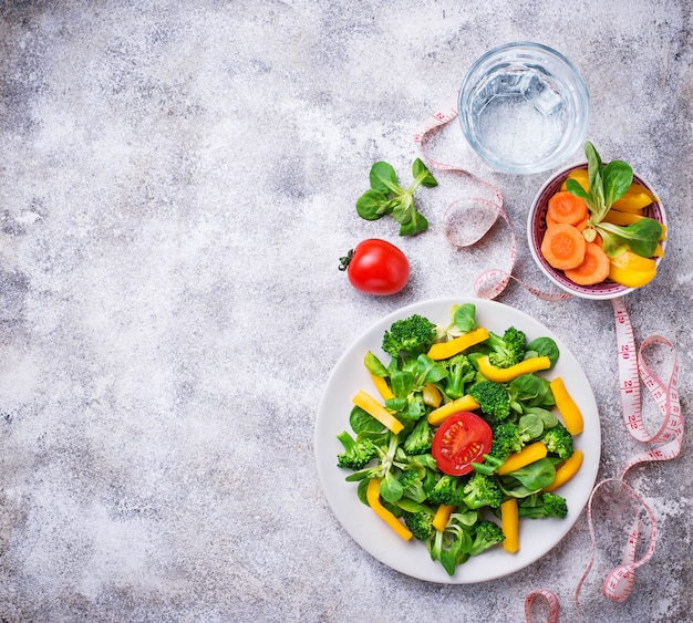 Insalata di verdure sana, acqua e nastro di misurazione