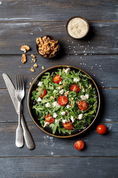 Insalata di verdure sana con rucola, pomodoro, feta e noci freschi sul piatto scuro. Menu dietetico