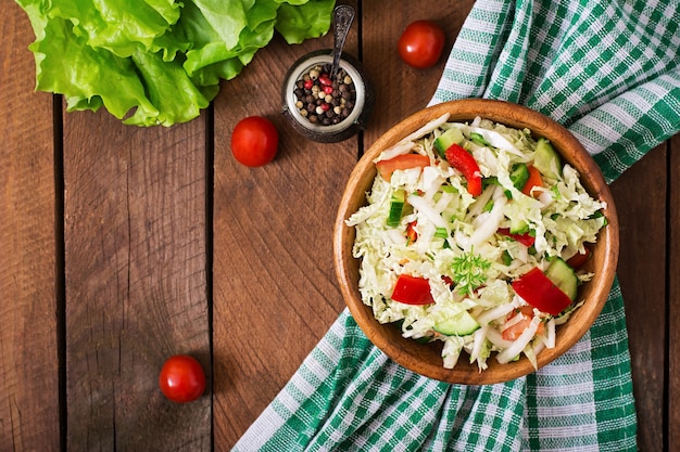 Insalata di verdure vegetali (cavolo, pomodoro, paprica, cetriolo, cipolla) in una ciotola di legno