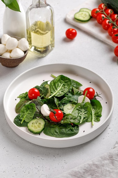 Insalata di verdure verdi con foglie di insalata mista, spinaci, pomodori e mozzarella su piatto bianco. Olio su fondo.