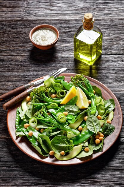 Insalata di verdure verdi di gambo tenero saltato broccoli mangetout avocado cetriolo ceci spinaci con olio d'oliva condimento servito su un piatto di argilla marrone su un tavolo scuro primo piano vista dall'alto