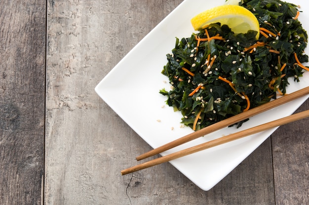 Insalata di Wakame con carota, semi di sesamo e succo di limone nel piatto sul tavolo di legno