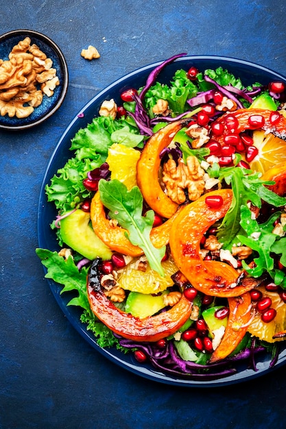 Insalata di zucca autunnale con fette di zucca caramellate cavolo rosso avocado rucola semi di melograno e noci Sano vegan vegetariano mangiare comfort food Sfondo blu Vista dall'alto