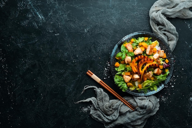 Insalata di zucca con carne di pollo e verdure in un piatto nero su sfondo nero Vista dall'alto Spazio libero per il testo