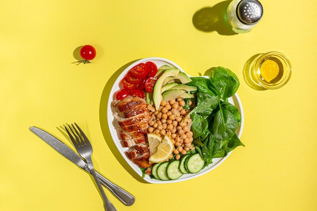 Insalata dietetica con pollo avocado cetriolo pomodoro e spinaci su sfondo giallo Disposizione piatta Luce intensa
