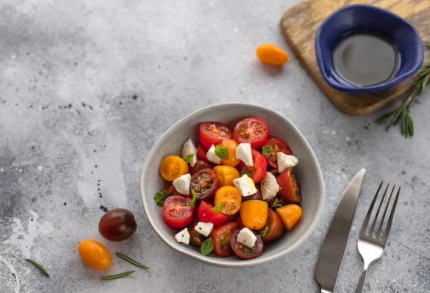 Insalata dietetica con pomodorini freschi, formaggio feta, rosmarino e olio d'oliva concetto sano vegiterian superficie in cemento grigio,