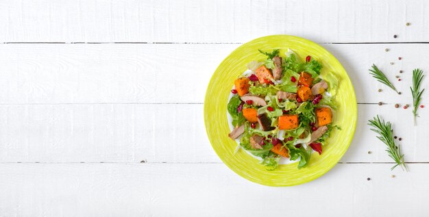 Insalata dietetica con tacchino arrosto, zucca e lattuga verde su un legno bianco