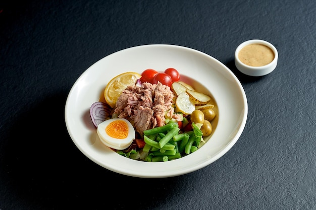 Insalata dietetica nizzarda con tonno, uova e asparagi in un piatto bianco su sfondo nero