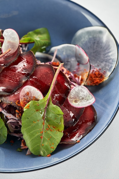 Insalata estiva di barbabietola con rucola, radicchio, formaggio a pasta molle e noci su condimento per piatti e spezie su piatto blu, copia spazio, vista dall'alto.