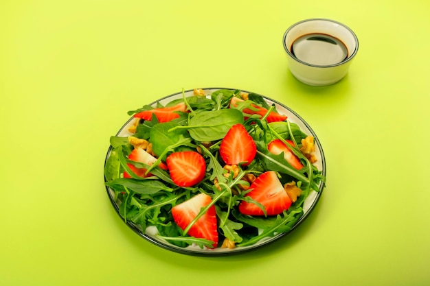 Insalata estiva di fragole con spinaci foglie di rucola noci e aceto balsamico e olio d'oliva condimento su sfondo verde avocado Concetto di cibo sano Vista dall'alto spazio di copia