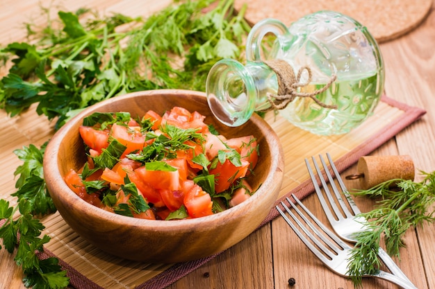 Insalata fatta di pomodori ed erbe fresche, olio e forchetta sul tavolo di legno