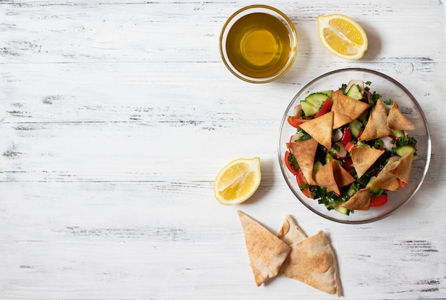 Insalata Fattoush tradizionale con verdure e pane pita. Cucina levantina, araba, mediorientale. Servito in una lastra di vetro con limone, pita e olio d'oliva. Sfondo chiaro. Vista dall'alto. Spazio per il testo