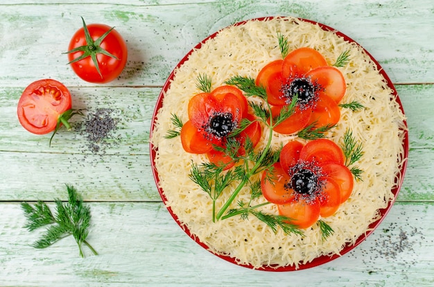 Insalata festiva cosparsa di formaggio grattugiato e decorata con papaveri a base di pomodori e olive a fette. Arte-cibo