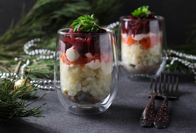 Insalata festiva russa tradizionale Aringa sotto una pelliccia in bicchieri porzionati su uno sfondo di Capodanno