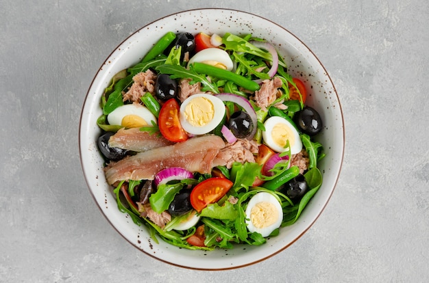 Insalata francese Nicoise con tonno, pomodori, olive, lattuga e altro su una ciotola su sfondo di cemento