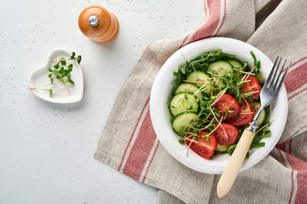 Insalata fresca con pomodoro, cetriolo, verdure, ravanelli microgreen in piatto bianco su pietra grigia