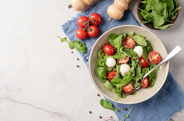 Insalata fresca con rucola pomodorini mozzarella e formaggio a pasta dura su fondo di legno bianco Vista dall'alto