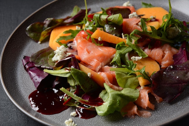 Insalata fresca con salmone, cachi, rucola e anacardi. Servito con salsa al miele di melograno