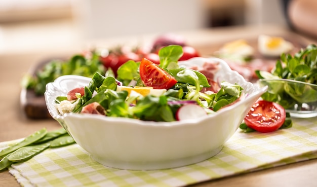 Insalata fresca di primavera con foglie verdi pomodori uova ravanelli cipolla rossa piselli novelli prosciutto feta e olio d'oliva.