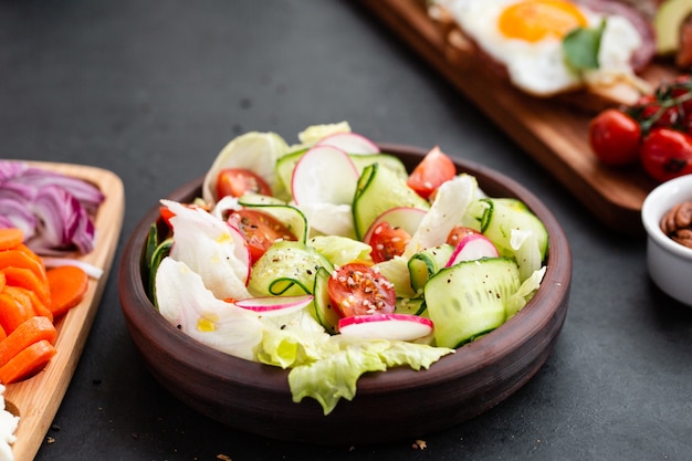 Insalata fresca di verdure classica sana di lattuga, del pomodoro, del cetriolo, della cipolla e del sesamo con il condimento dell'olio d'oliva sulla banda nera e sul gray.