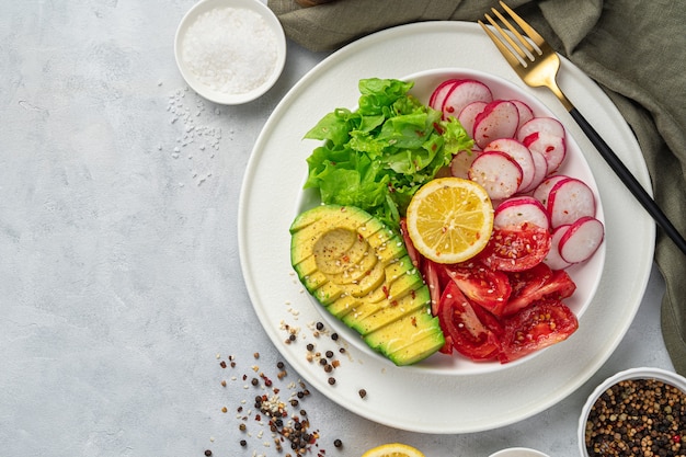 Insalata fresca e estiva con avocado, pomodoro e ravanello su un tavolo grigio.