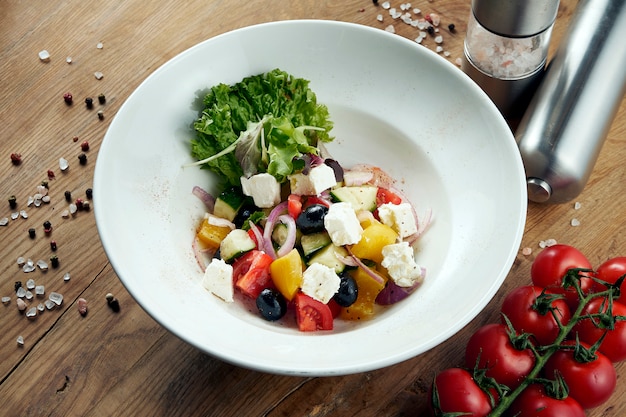 Insalata greca classica con pomodori, cipolle, cetrioli, formaggio feta e olive nere in pita su un piatto bianco.