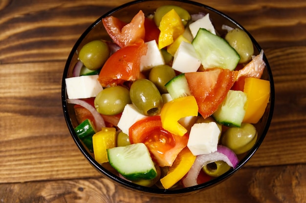 Insalata greca con formaggio feta di verdure fresche e olive verdi in ciotola di vetro su tavola di legno