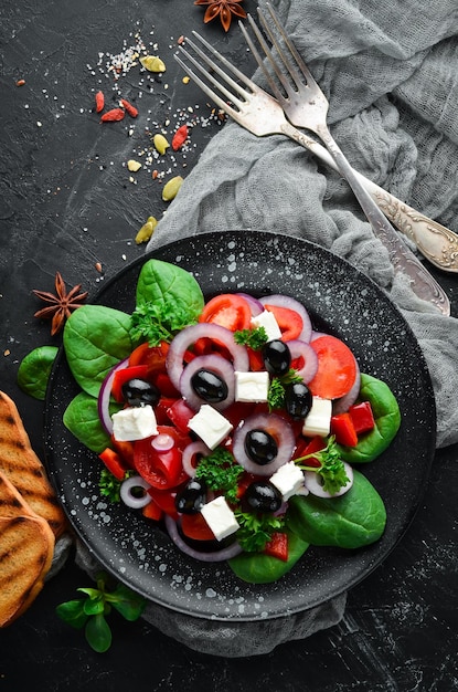 Insalata greca con pomodori paprika cipolle e formaggio feta In un piatto nero su sfondo di legno Vista dall'alto Spazio libero per il testo Disposizione piatta