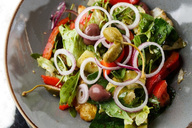 Insalata greca con verdure fresche pomodoro cetriolo peperone rosso lattuga cipolla olive e formaggio Primo piano su un piatto rotondo bianco su fondo di legno Menu di insalata con ingredienti