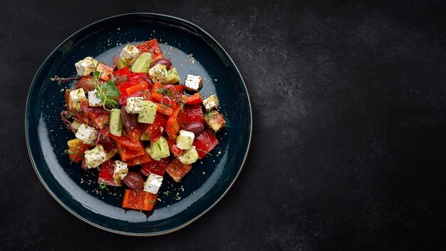 Insalata greca con verdure, olive e formaggio su un piatto scuro su cemento scuro