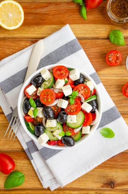 Insalata greca di verdure fresche e succose, formaggio feta, erbe aromatiche e olive in una ciotola bianca su un legno