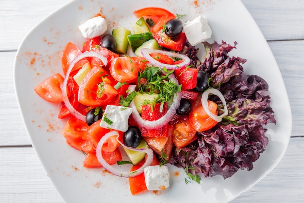 Insalata greca fresca con la cipolla sul piatto bianco e sulla tavola di legno