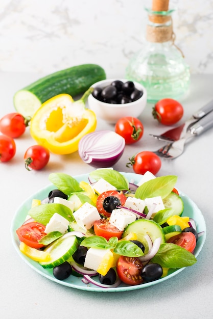 Insalata greca fresca fatta in casa con foglie di basilico su un piatto e ingredienti per cucinare sul tavolo