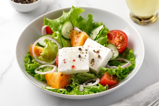 Insalata greca in ciotola bianca Insalata di verdure con pomodoro cipolla cetrioli pepe lattuga formaggio feta