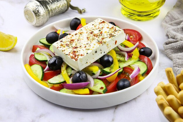 Insalata greca in un piatto su uno sfondo di marmo grigio. Piatto da ristorante. Insalata di verdure con olio d'oliva