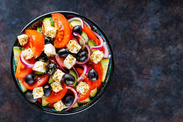 Insalata greca in una ciotola su uno sfondo scuro. Insalata sana con formaggio feta e olive. Insalata di verdure fresche della cucina mediterranea. Copia spazio. Vista dall'alto