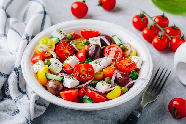 Insalata greca tradizionale con cetriolo fresco, pomodoro, lattuga, capperi, cipolla rossa, feta, formaggio e olive