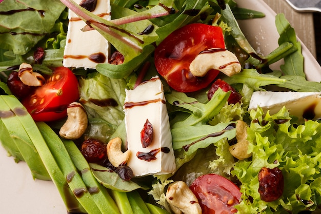 Insalata gustosa e salutare con rucola, brie, formaggio, avocado, pomodorini, mirtilli rossi secchi e anacardi.