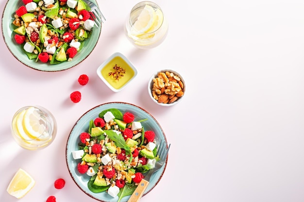 Insalata leggera con lampone, spinaci, formaggio feta, avocado e noci, vista dall'alto Insalata estiva fresca e originale con acqua di limone su spazio rosa per la copia del tavolo