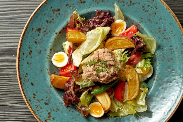 Insalata nizzarda con tonno e patate in un piatto blu su fondo di legno