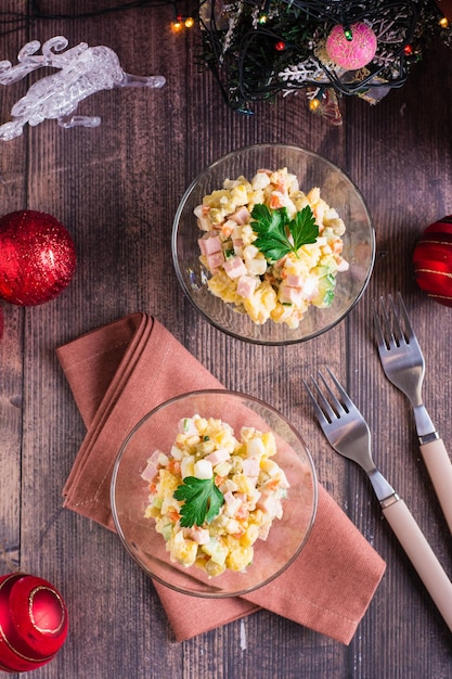 Insalata Olivier in ciotole e decorazioni natalizie su un tavolo di legno Vista superiore e verticale