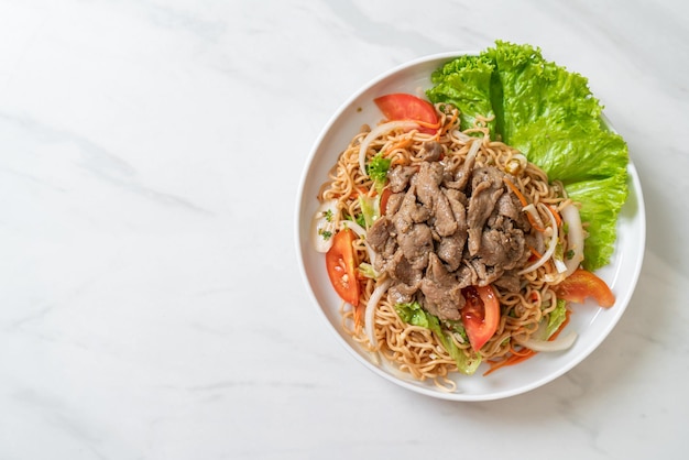 insalata piccante di noodle istantanei con carne di maiale su piatto bianco - stile asiatico dell'alimento