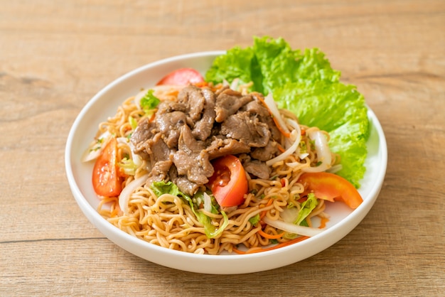 insalata piccante di noodle istantanei con carne di maiale sul piatto bianco - stile di cibo asiatico